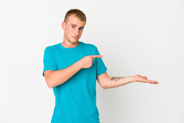 Young caucasian handsome man excited holding a copy space on palm.