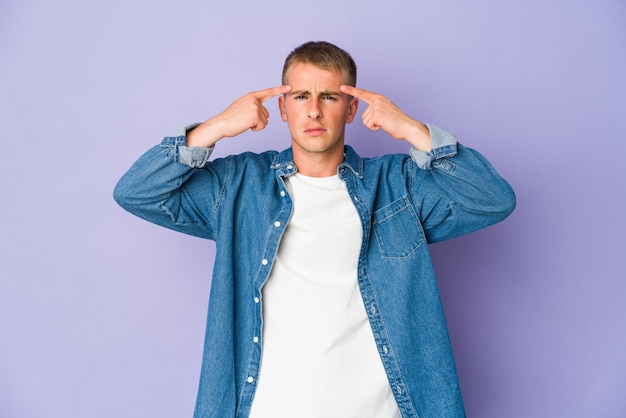 Young caucasian handsome man focused on a task, keeping forefingers pointing head.