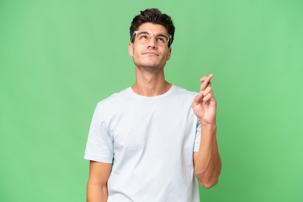 Young caucasian handsome man over isolated background with fingers crossing and wishing the best