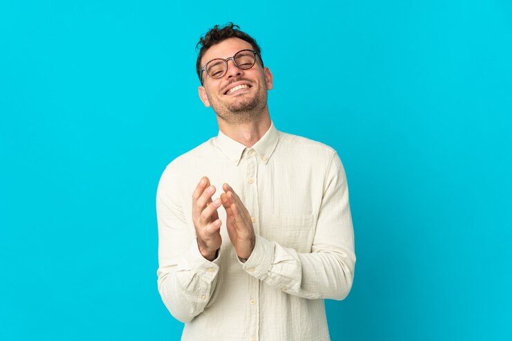 Photo young caucasian handsome man isolated on blue background applauding after presentation in a conference