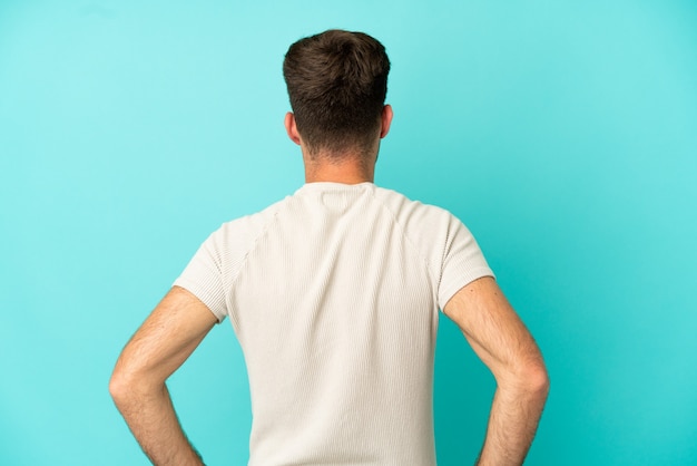 Young caucasian handsome man isolated on blue background in back position