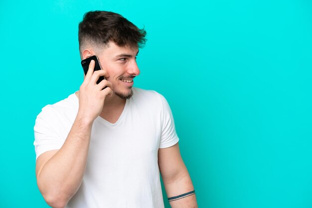 Young caucasian handsome man isolated on blue background keeping a conversation with the mobile phone with someone