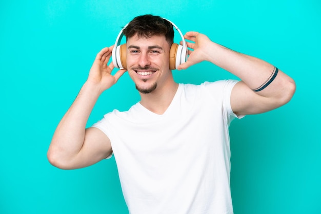 Giovane uomo bello caucasico isolato su sfondo blu ascoltando musica