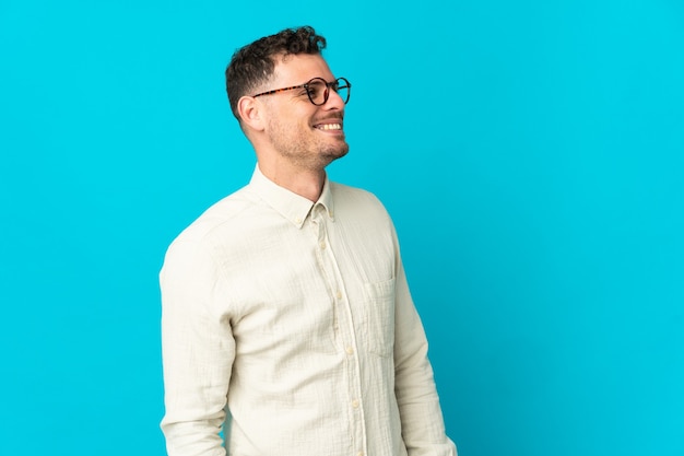 Young caucasian handsome man isolated on blue background looking to the side and smiling