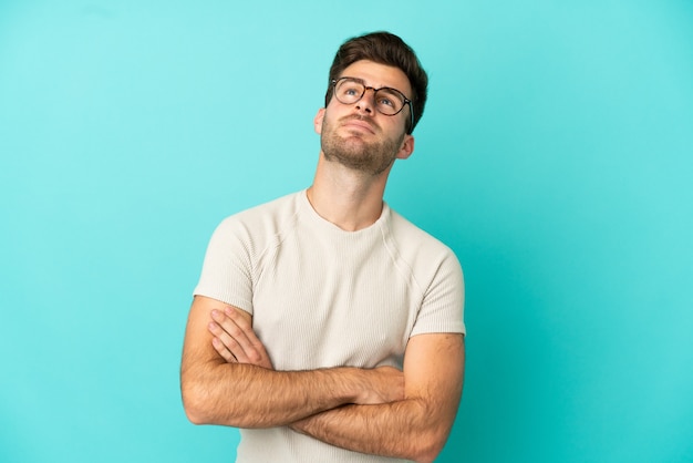 Young caucasian handsome man isolated on blue background looking up while smiling