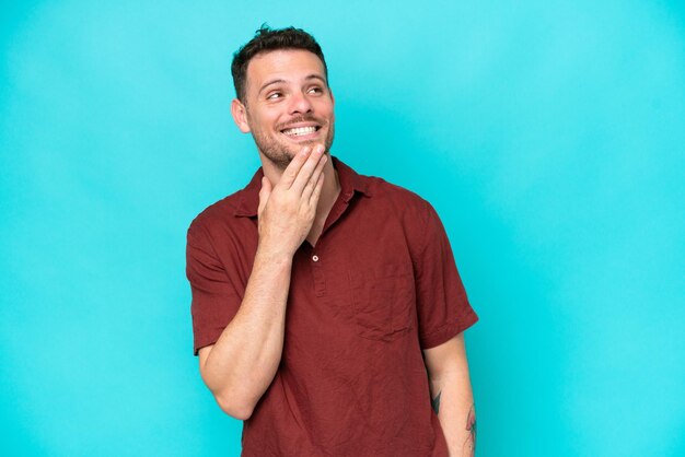 Young caucasian handsome man isolated on blue background looking up while smiling