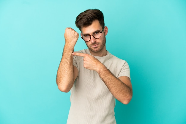 Giovane uomo caucasico bello isolato su sfondo blu che fa il gesto di essere in ritardo