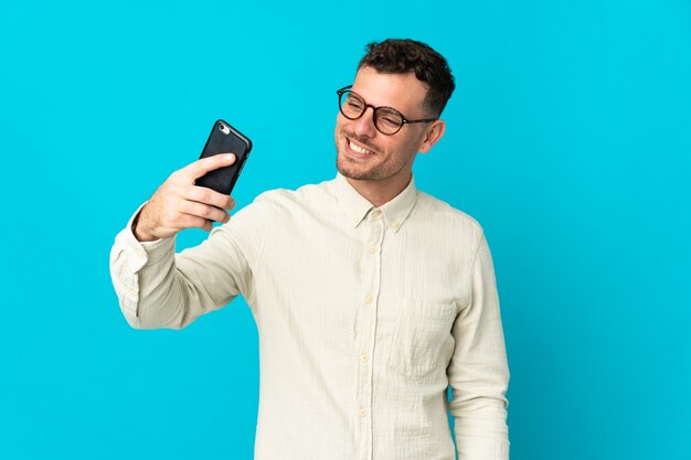 Young caucasian handsome man isolated on blue background making a selfie