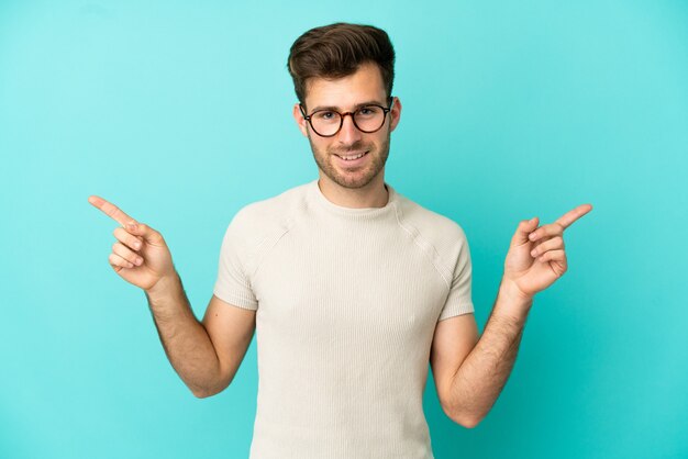 Young caucasian handsome man isolated on blue background pointing finger to the laterals and happy