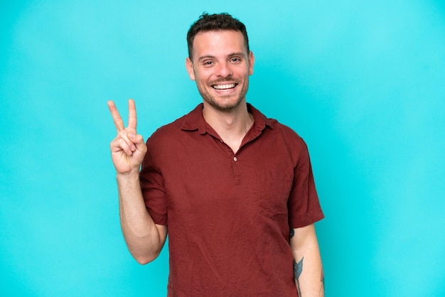 Young caucasian handsome man isolated on blue background smiling and showing victory sign