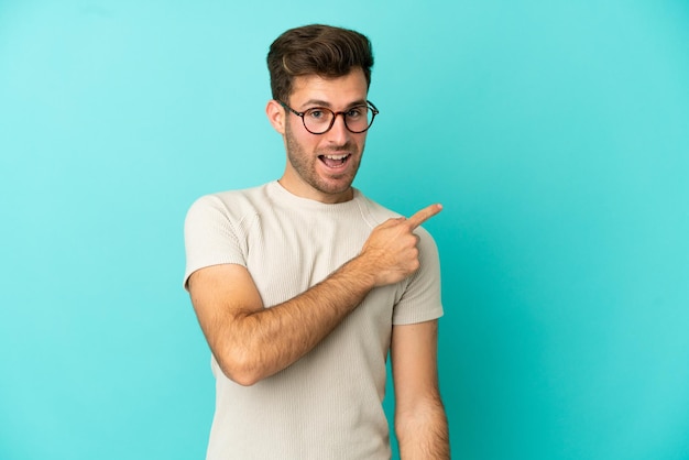 Young caucasian handsome man isolated on blue background surprised and pointing side