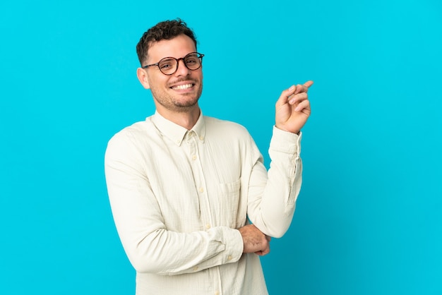 Young caucasian handsome man isolated on blue pointing finger to the side