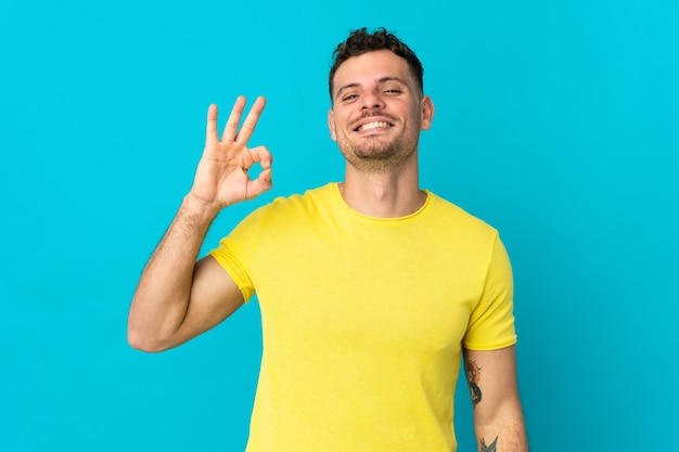 Young caucasian handsome man isolated on blue showing ok sign with fingers