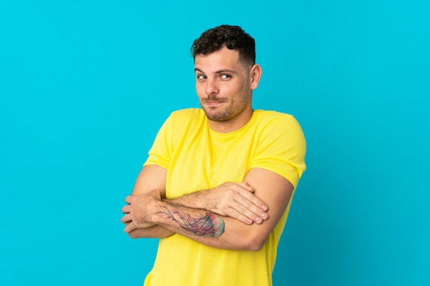 Young caucasian handsome man isolated on blue wall making doubts gesture while lifting the shoulders