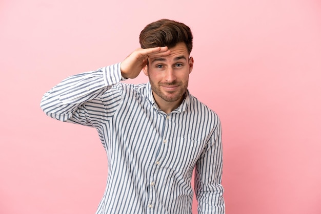 Foto giovane uomo caucasico bello isolato su sfondo rosa che guarda lontano con la mano per guardare qualcosa