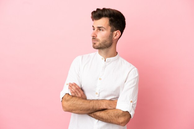 Young caucasian handsome man isolated on pink background looking to the side