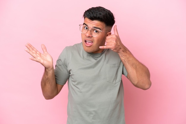 Young caucasian handsome man isolated on pink background making phone gesture and doubting