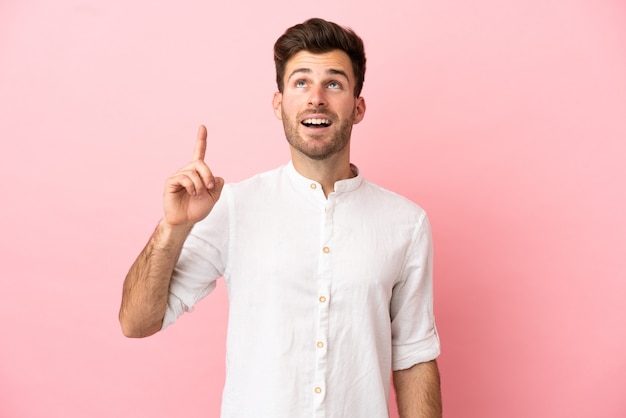 Young caucasian handsome man isolated on pink background pointing up and surprised