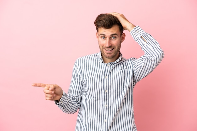 Young caucasian handsome man isolated on pink background surprised and pointing finger to the side