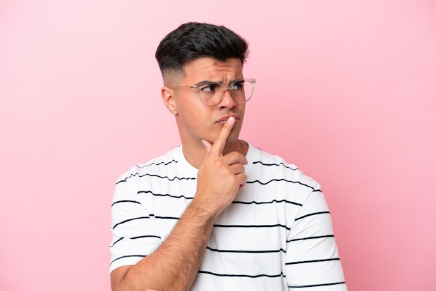Young caucasian handsome man isolated on pink background With glasses and having doubts