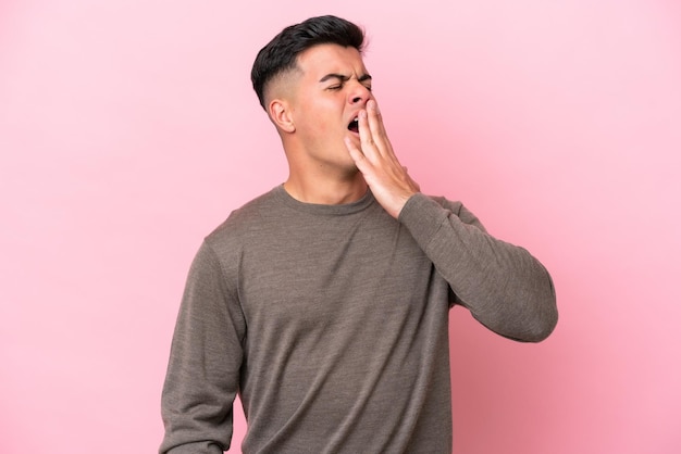 Young caucasian handsome man isolated on pink background yawning and covering wide open mouth with hand