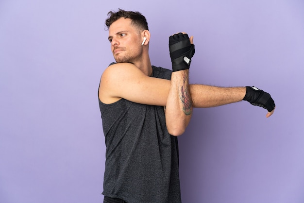 Photo young caucasian handsome man isolated on purple background stretching arm