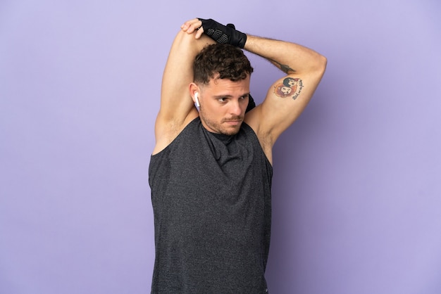 Young caucasian handsome man isolated on purple wall stretching arm