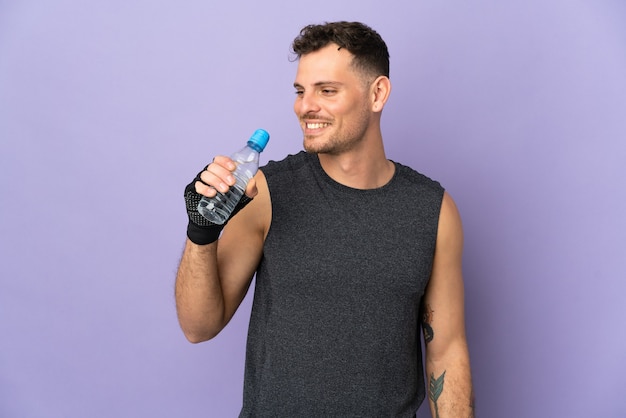 Young caucasian handsome man isolated on purple with sports water bottle