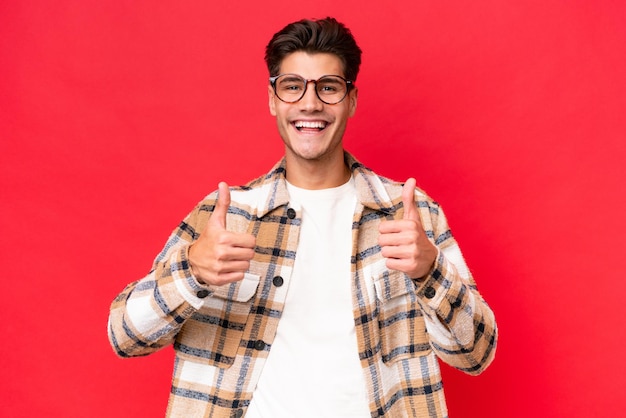 Young caucasian handsome man isolated on red background giving a thumbs up gesture