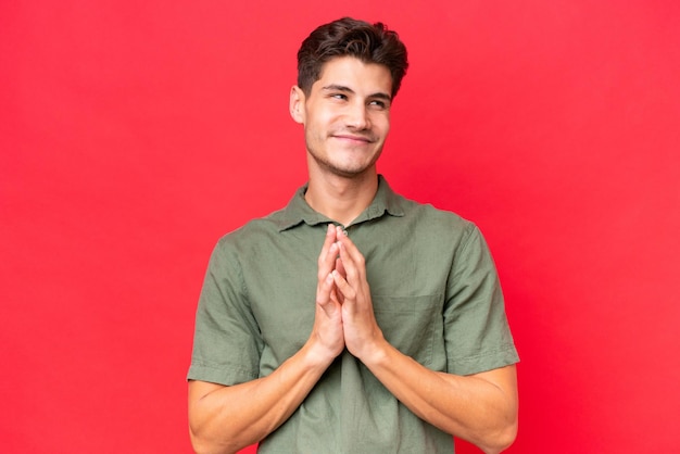 Young caucasian handsome man isolated on red background scheming something