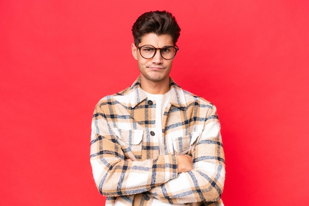 Young caucasian handsome man isolated on red background with unhappy expression