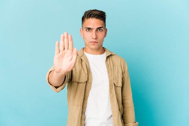 Young caucasian handsome man isolated standing with outstretched hand showing stop sign, preventing you.