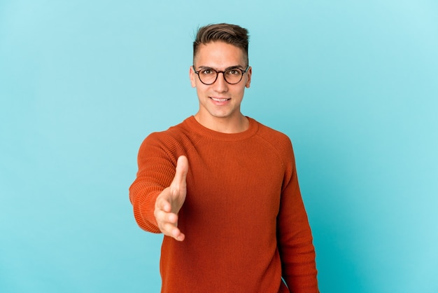 Young caucasian handsome man isolated stretching hand at camera in greeting gesture.