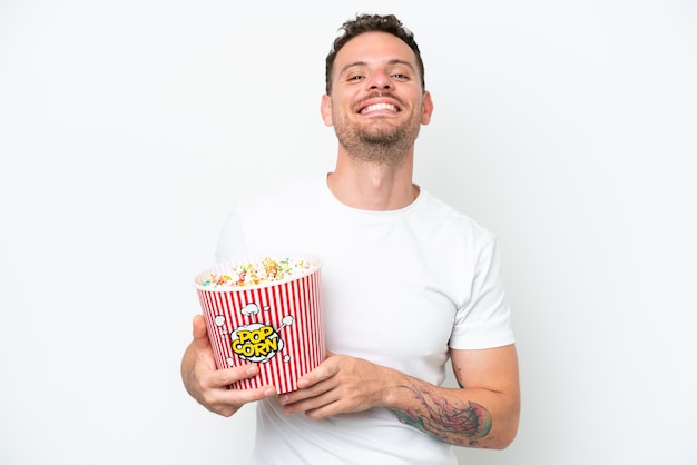 Young caucasian handsome man isolated on white background holding a big bucket of popcorns