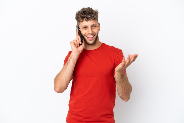 Young caucasian handsome man isolated on white background keeping a conversation with the mobile phone with someone