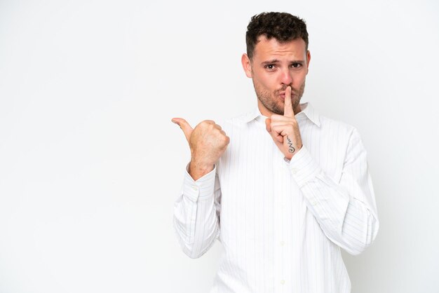 Young caucasian handsome man isolated on white background pointing to the side and doing silence gesture