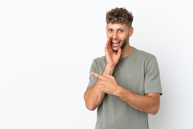 Young caucasian handsome man isolated on white background pointing to the side to present a product and whispering something