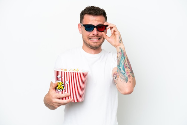 Young caucasian handsome man isolated on white background with 3d glasses and holding a big bucket of popcorns