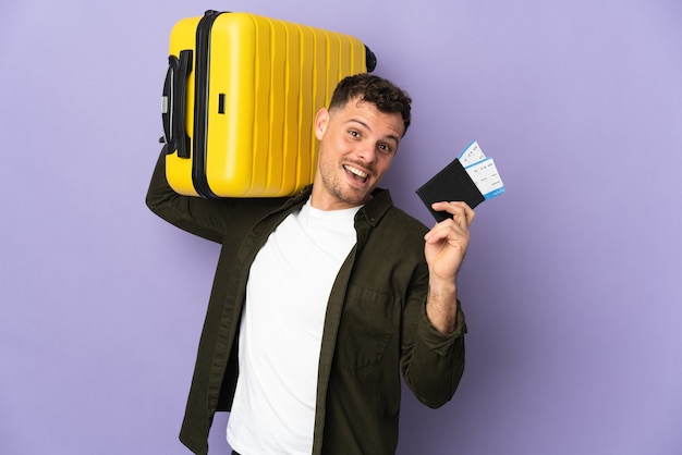 Young caucasian handsome man isolated on white wall in vacation with suitcase and passport