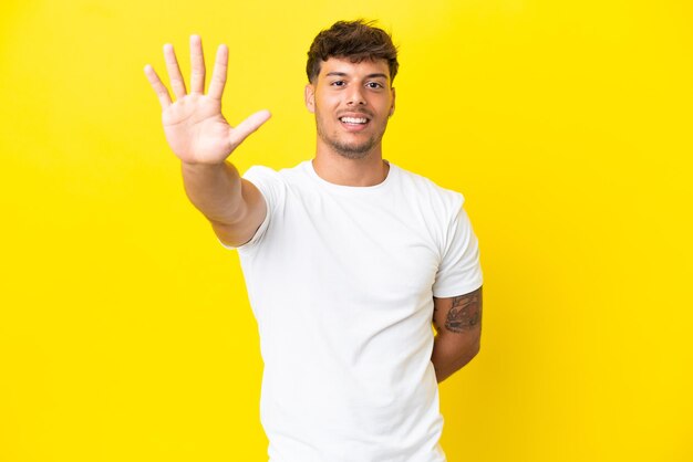 Young caucasian handsome man isolated on yellow background counting five with fingers