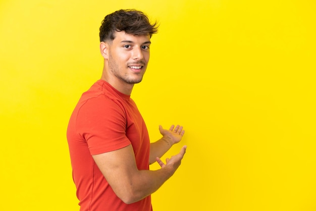 Young caucasian handsome man isolated on yellow background extending hands to the side for inviting to come