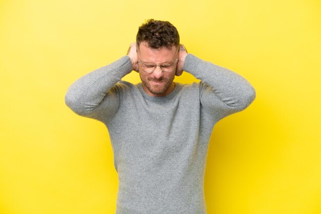 Young caucasian handsome man isolated on yellow background frustrated and covering ears