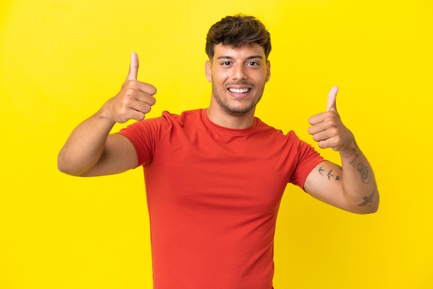 Young caucasian handsome man isolated on yellow background giving a thumbs up gesture