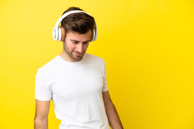音楽を聴いて黄色の背景に分離された若い白人ハンサムな男