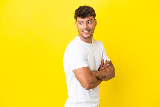 Young caucasian handsome man isolated on yellow background looking to the side and smiling