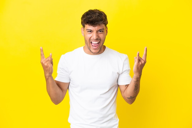 Young caucasian handsome man isolated on yellow background making horn gesture