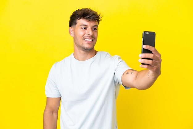 Молодой кавказский красавец изолирован на желтом фоне, делая селфи с мобильным телефоном