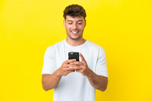 Young caucasian handsome man isolated on yellow background sending a message or email with the mobile