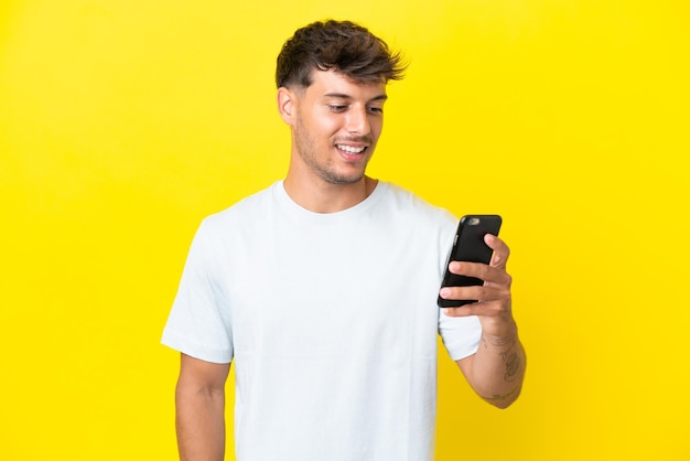 携帯電話でメッセージやメールを送信する黄色の背景に分離された若い白人ハンサムな男