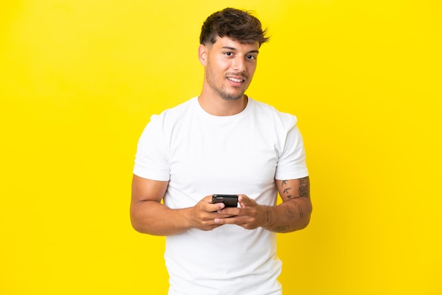 Young caucasian handsome man isolated on yellow background sending a message with the mobile